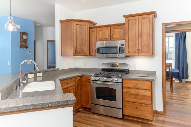 kitchen with stainless steel appliances, dark countertops, a sink, and wood finished floors