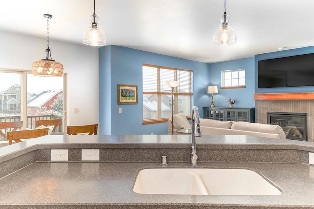 kitchen featuring a tiled fireplace, a sink, and decorative light fixtures