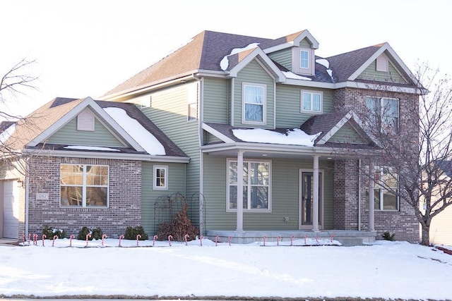 view of front of house with covered porch, brick siding, and roof with shingles