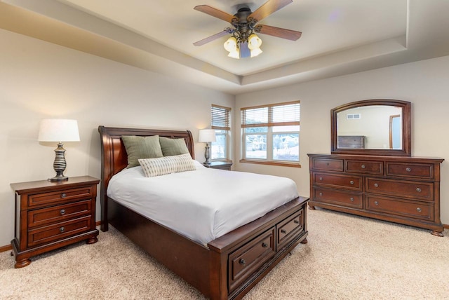 bedroom with light carpet, ceiling fan, a tray ceiling, and visible vents