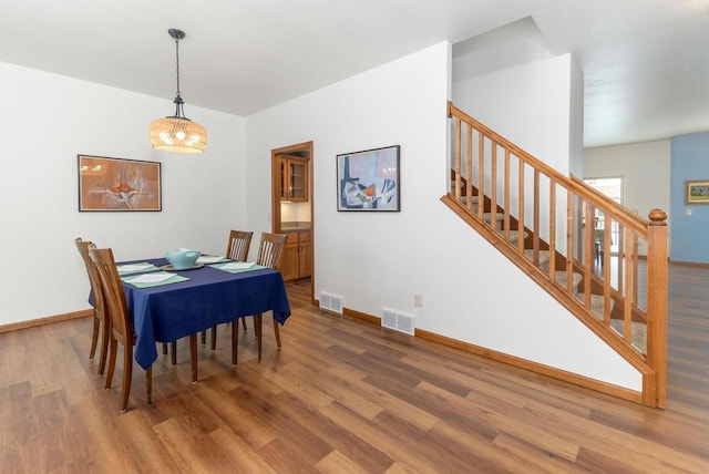 dining space with stairs, visible vents, baseboards, and wood finished floors