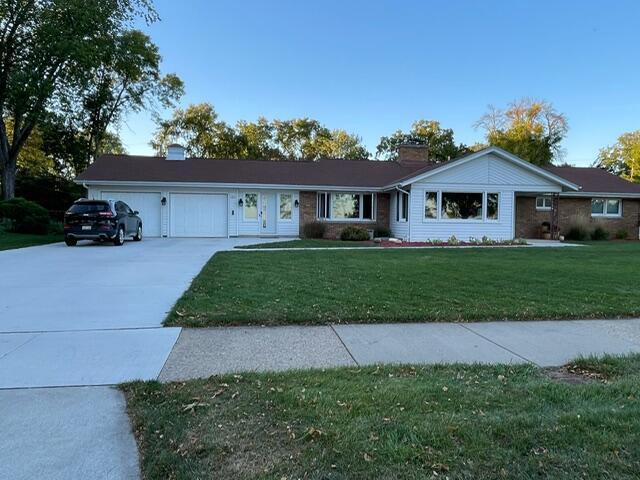 ranch-style house featuring driveway, a chimney, an attached garage, and a front yard