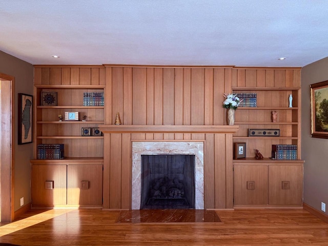 unfurnished living room featuring light wood-style floors, built in shelves, baseboards, and a high end fireplace