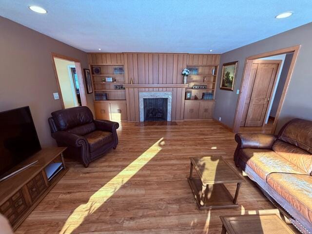 living area featuring built in shelves, wood finished floors, a high end fireplace, and recessed lighting