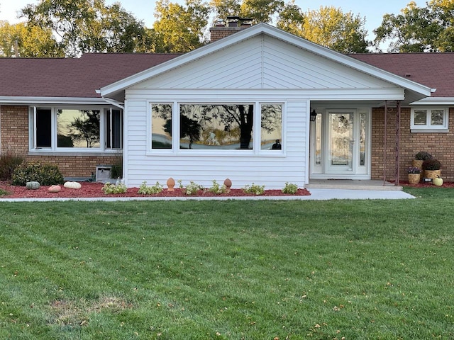 view of front facade featuring a front yard, a chimney, and brick siding