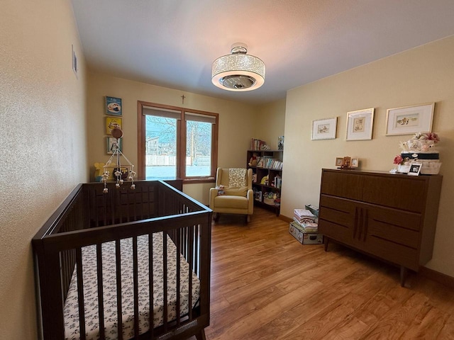 bedroom featuring light wood-type flooring, baseboards, visible vents, and a nursery area