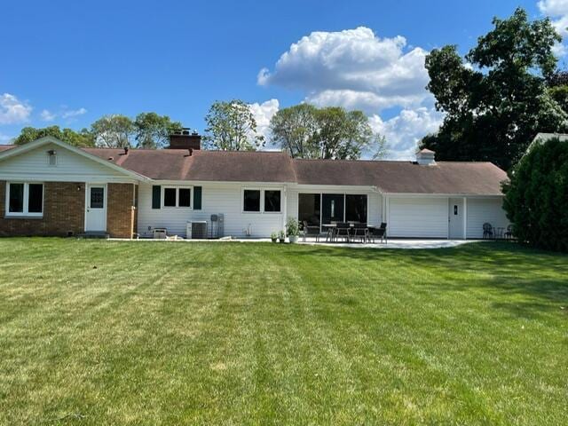 back of property with a garage, a lawn, a chimney, and central AC unit