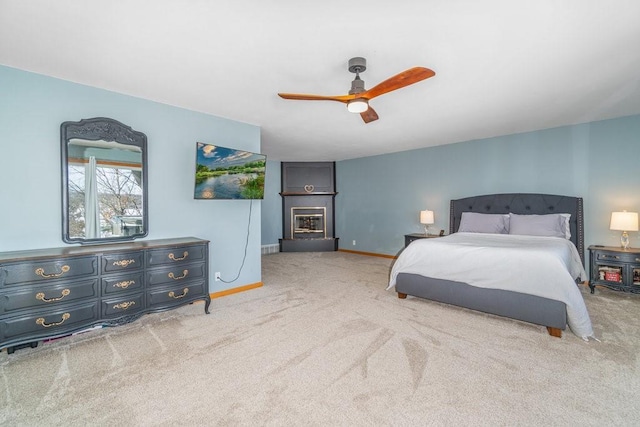 bedroom with baseboards, light colored carpet, a ceiling fan, and a glass covered fireplace