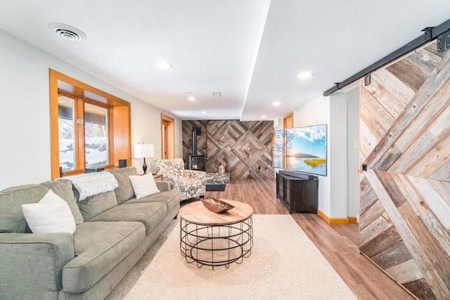 living room featuring a barn door, visible vents, an accent wall, a wood stove, and light wood-style floors