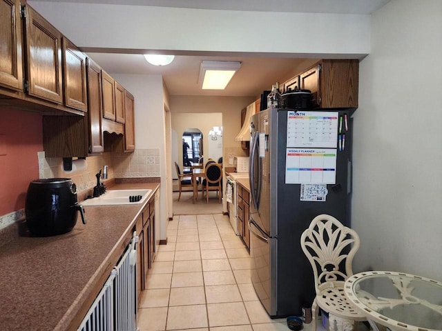 kitchen featuring light tile patterned floors, arched walkways, a sink, freestanding refrigerator, and tasteful backsplash