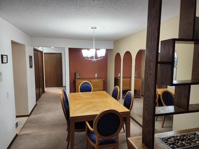 dining space featuring arched walkways, light colored carpet, a notable chandelier, and a textured ceiling