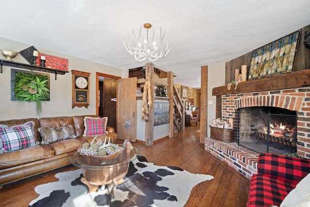 living room with stairs, a brick fireplace, wood finished floors, and a chandelier