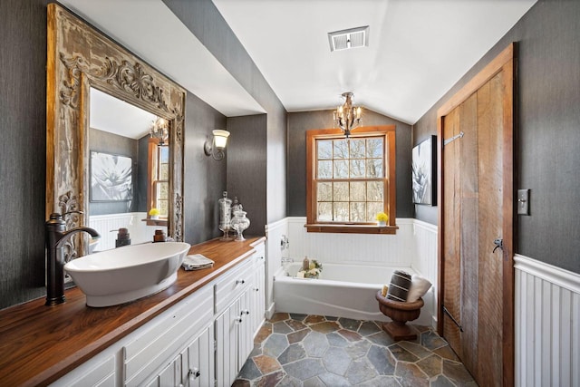 bathroom with lofted ceiling, visible vents, a bath, and wainscoting