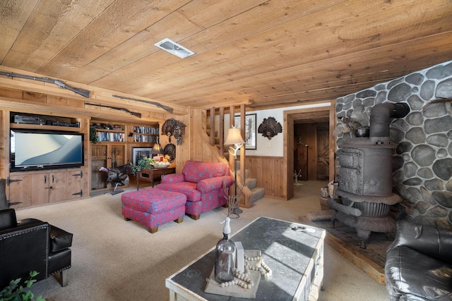 carpeted living area with wooden ceiling, wooden walls, visible vents, stairway, and a wood stove