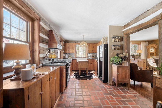 kitchen featuring brick floor, light countertops, freestanding refrigerator, brown cabinetry, and pendant lighting