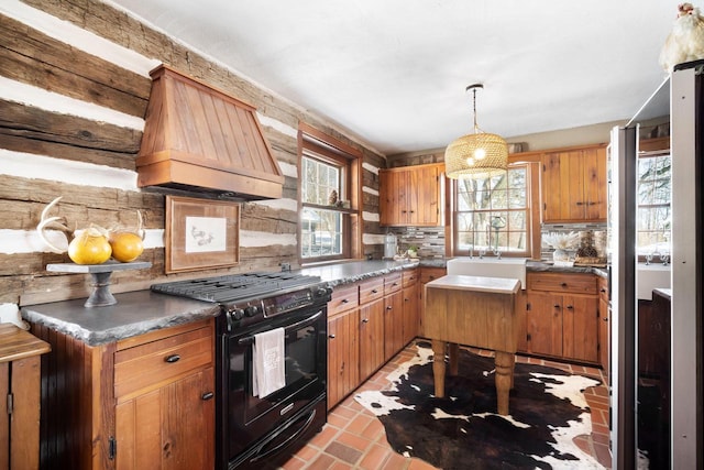 kitchen featuring black gas range oven, dark countertops, brown cabinets, custom exhaust hood, and pendant lighting