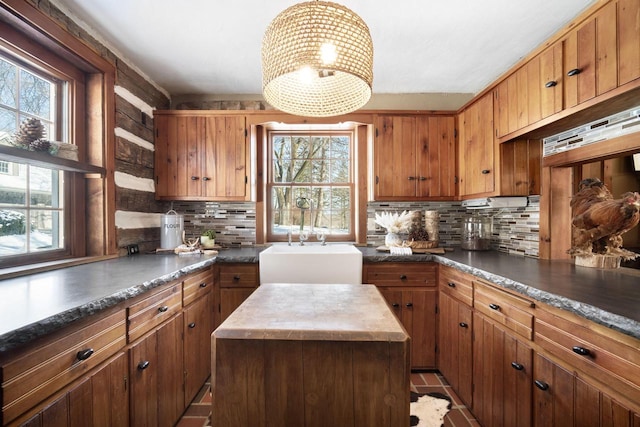 kitchen featuring brown cabinetry, dark countertops, a kitchen island, and a sink