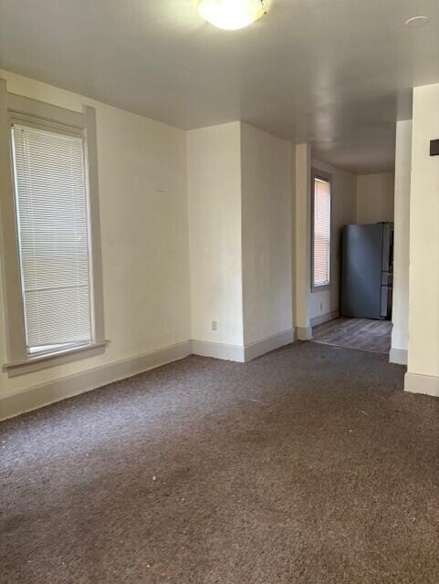 spare room featuring dark colored carpet and baseboards