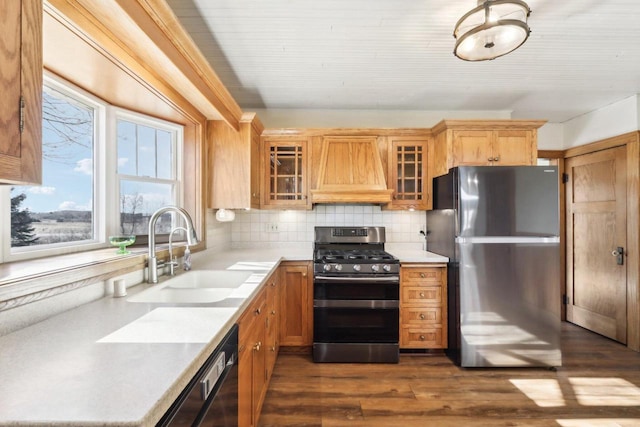 kitchen featuring custom range hood, glass insert cabinets, appliances with stainless steel finishes, light countertops, and a sink