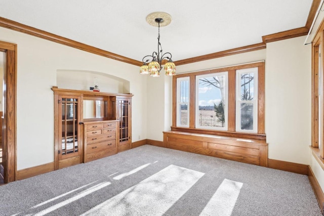 unfurnished dining area featuring an inviting chandelier, carpet, baseboards, and crown molding