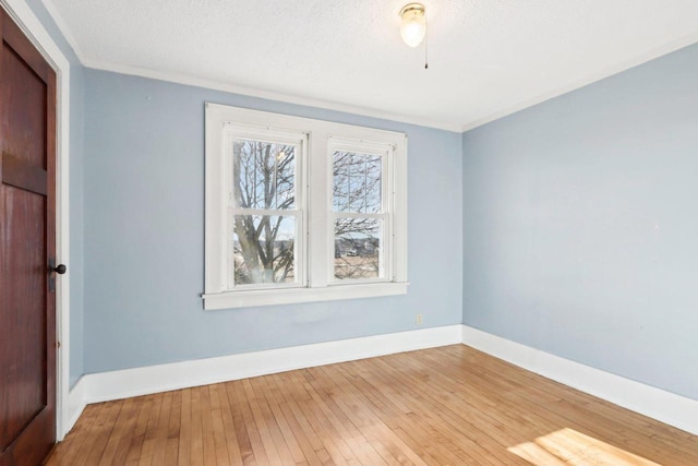 empty room with a textured ceiling, crown molding, wood finished floors, and baseboards