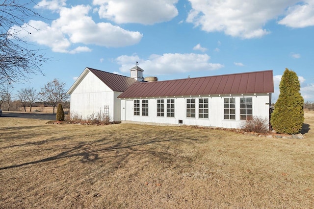 back of house with a standing seam roof, metal roof, a lawn, and a chimney