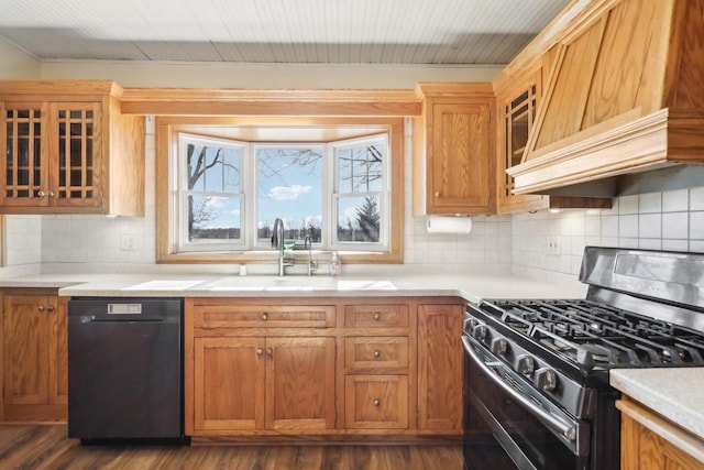 kitchen with glass insert cabinets, light countertops, black appliances, premium range hood, and a sink