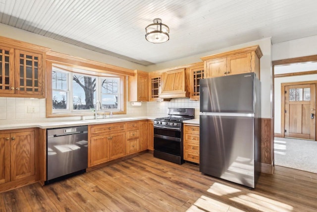 kitchen with appliances with stainless steel finishes, light countertops, premium range hood, and glass insert cabinets