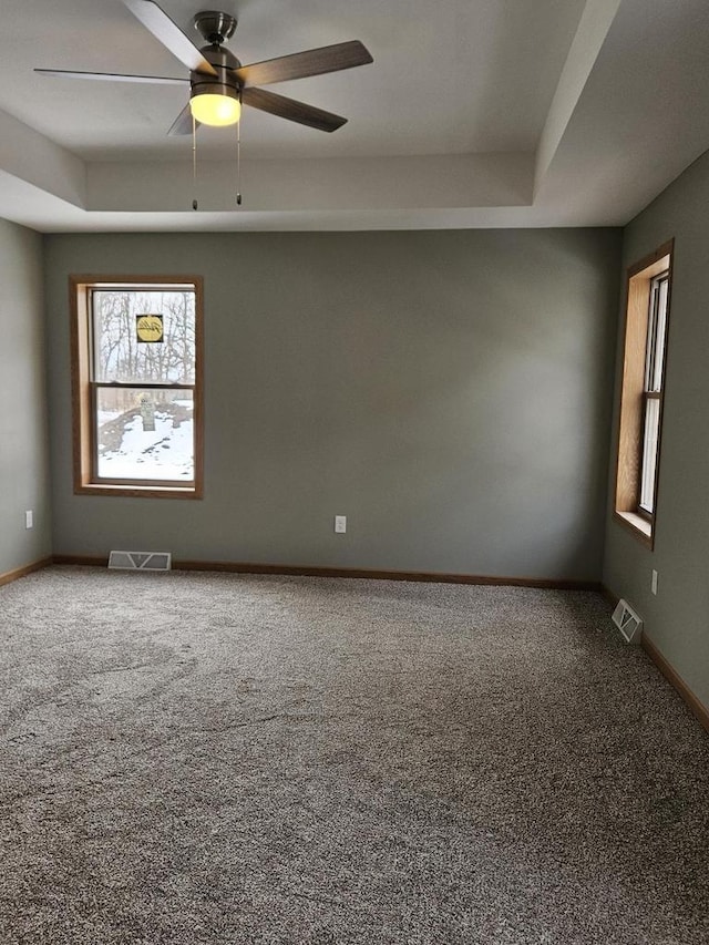 carpeted spare room with a ceiling fan, a raised ceiling, visible vents, and baseboards