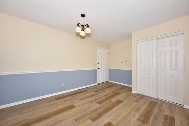 empty room featuring baseboards, wood finished floors, and an inviting chandelier