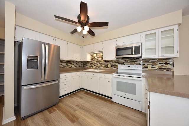 kitchen with stainless steel appliances, light wood-style flooring, glass insert cabinets, white cabinetry, and a sink