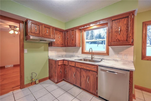 kitchen with a sink, under cabinet range hood, light countertops, and stainless steel dishwasher