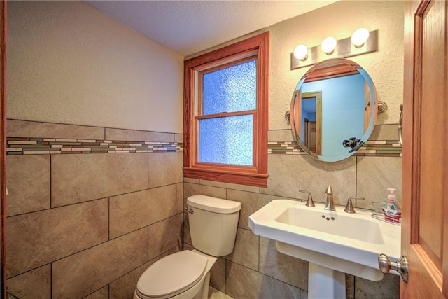 half bath featuring a textured wall, a sink, toilet, and tile walls