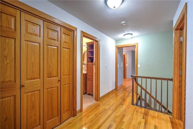 corridor featuring a textured ceiling, light wood finished floors, and an upstairs landing