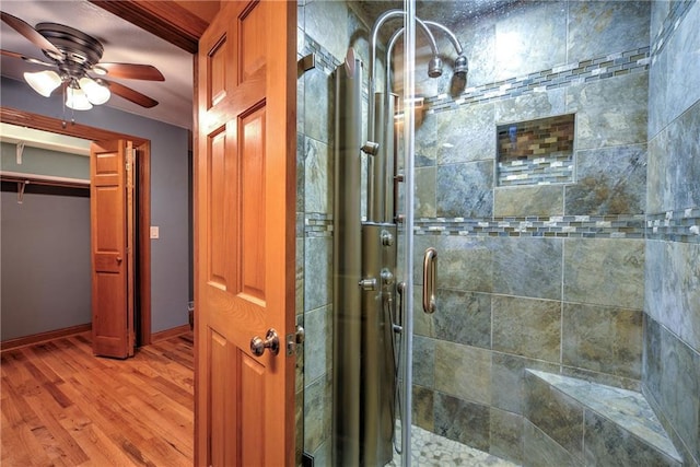 full bath with baseboards, a shower stall, a ceiling fan, and wood finished floors