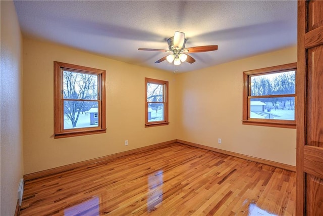 empty room featuring ceiling fan, a textured ceiling, light wood-type flooring, and baseboards