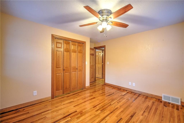 unfurnished bedroom with a closet, visible vents, light wood-style flooring, ceiling fan, and baseboards