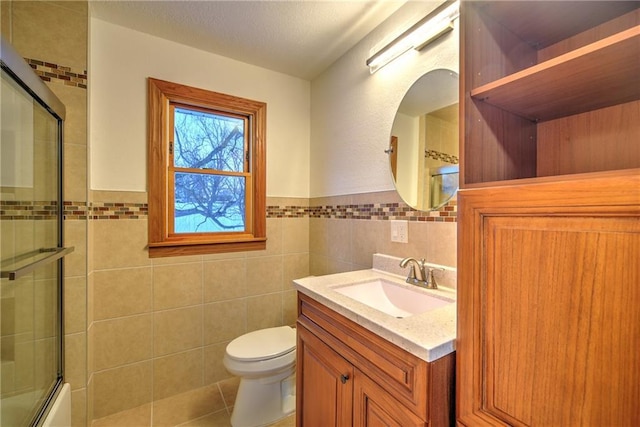 bathroom featuring toilet, enclosed tub / shower combo, tile patterned flooring, vanity, and tile walls