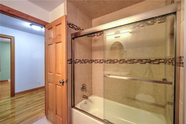 bathroom featuring wood finished floors, baseboards, and bath / shower combo with glass door