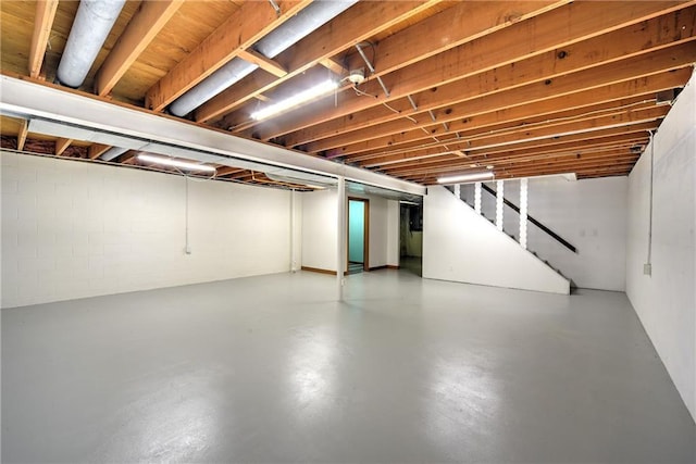 unfinished basement featuring stairway and concrete block wall