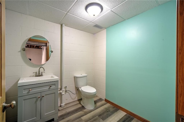 half bathroom with toilet, wood finished floors, visible vents, vanity, and concrete block wall