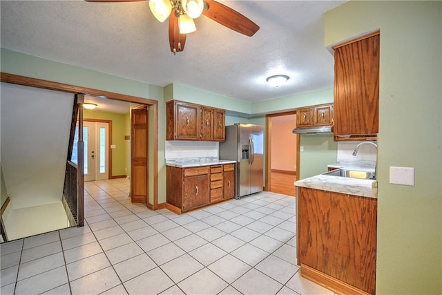 kitchen featuring light tile patterned floors, stainless steel fridge, brown cabinetry, light countertops, and a sink