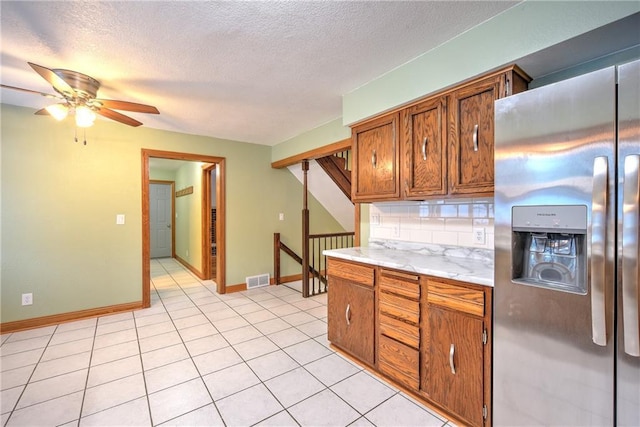 kitchen featuring brown cabinetry, backsplash, stainless steel refrigerator with ice dispenser, and light countertops