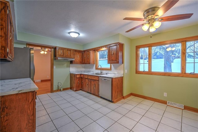 kitchen featuring visible vents, brown cabinetry, decorative backsplash, stainless steel appliances, and a sink