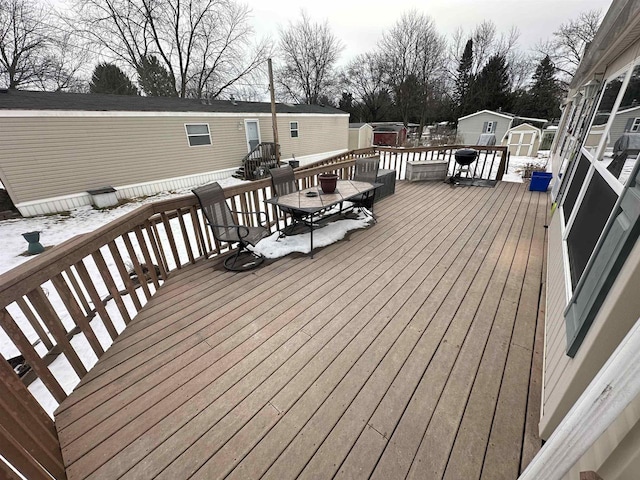 snow covered deck featuring a shed, an outbuilding, and outdoor dining space