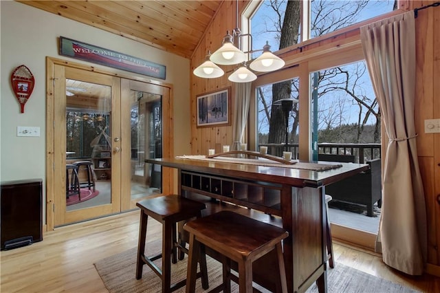 dining area with french doors, light wood-style floors, wood ceiling, vaulted ceiling, and wood walls