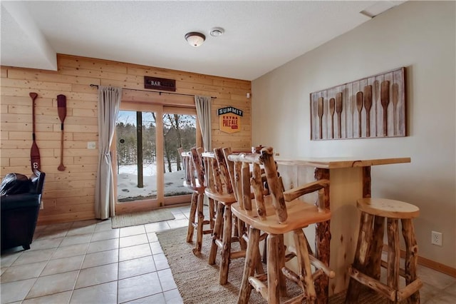 dining space with a bar, light tile patterned floors, wooden walls, and baseboards