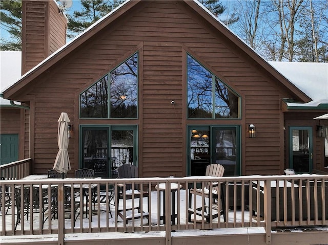 snow covered property with a chimney and a wooden deck