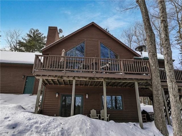 snow covered house with a chimney and a wooden deck