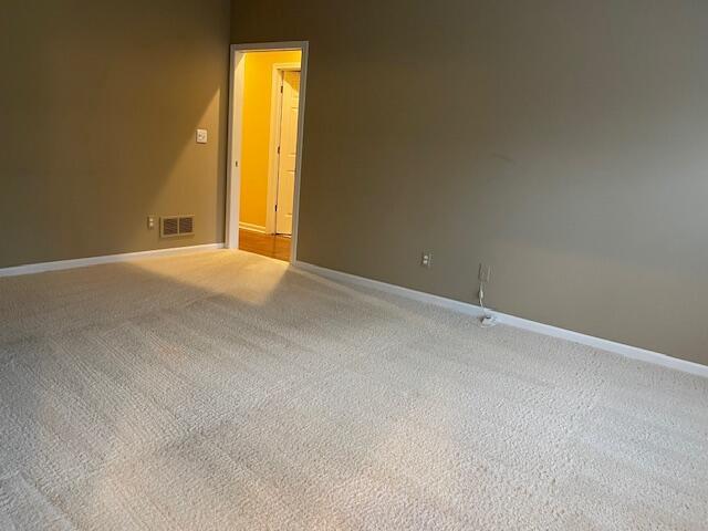 empty room with light carpet, visible vents, and baseboards